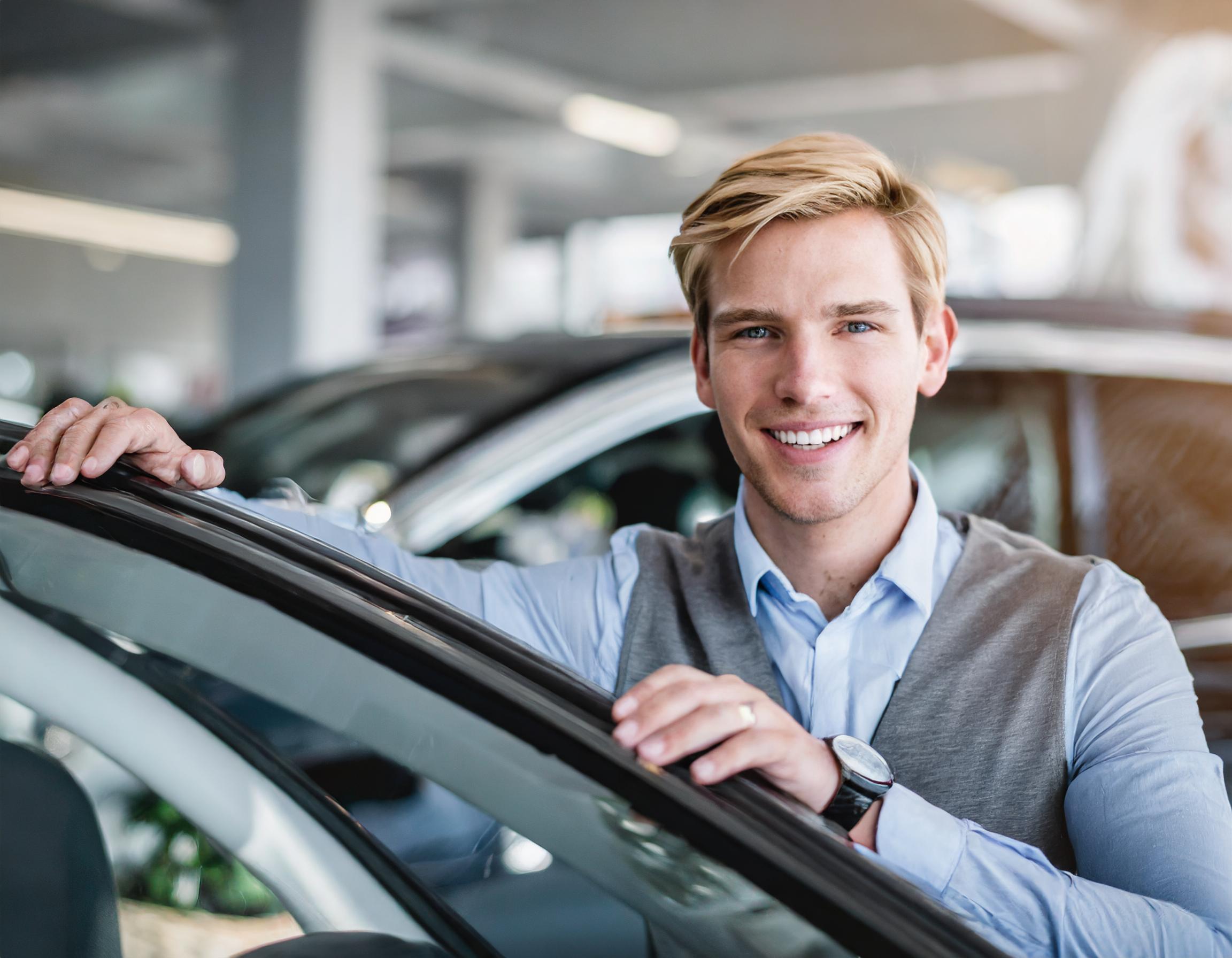 Ein zufriedener Kunde mit seinem neu erworbenen Fahrzeug vor dem Autohaus